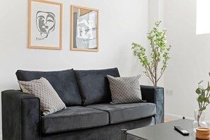 A modern living room with a grey sofa, two framed artworks, a small plant, and a remote control on a coffee table. - Warm and Inviting Apartment | Free Parking (Newark-on-Trent)