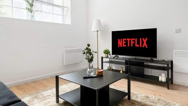 Een moderne woonkamer met een zwarte televisie, een salontafel, een lamp en een plant.