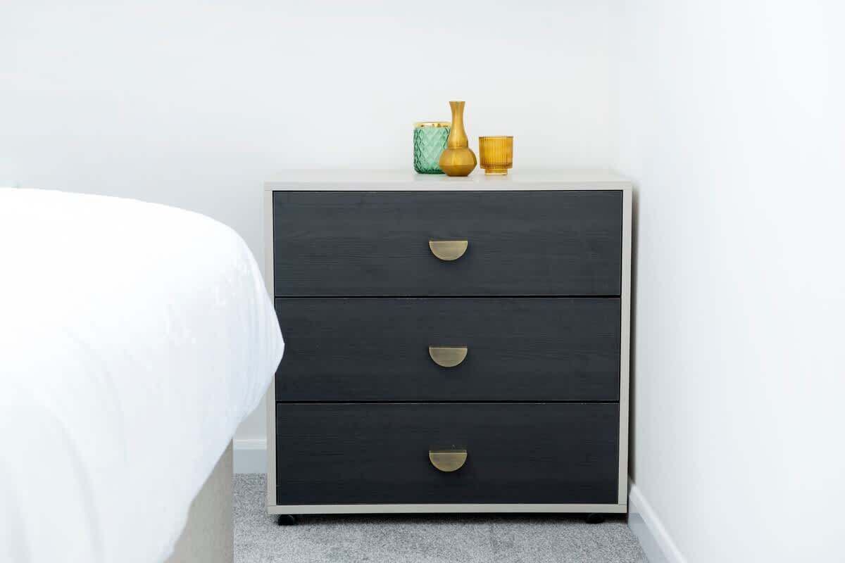 A dark wooden nightstand with three drawers and a small vase on top.
