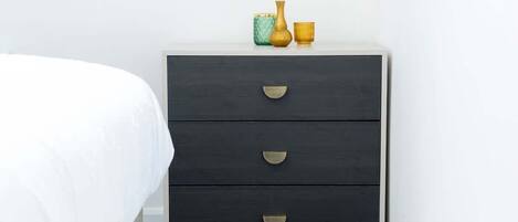A dark wooden nightstand with three drawers and a small vase on top.