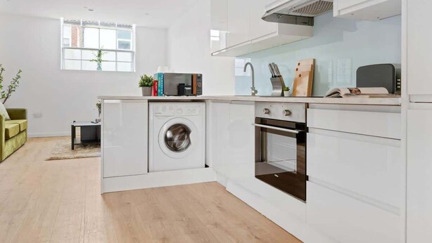 A compact kitchen with a washing machine, oven, and a small dining area with a table and chairs. - Charming Apartment | Free Parking and Wi-Fi (Newark-on-Trent)