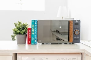 A microwave on a kitchen counter with a potted plant and books.