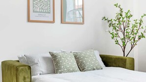 A bed with a white quilt, two patterned pillows, a green armchair, and a wall-mounted plant. - Charming Apartment | Free Parking and Wi-Fi (Newark-on-Trent)