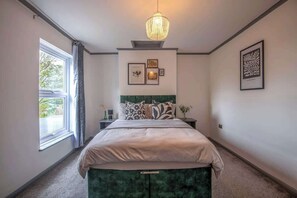 Un dormitorio con cama, ventana, cabecera verde y candelabro.