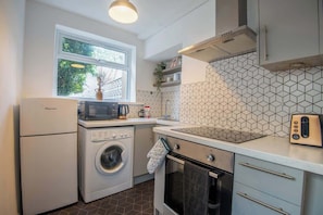 Une cuisine compacte équipée d’un lave-linge, d’un four, d’un four à micro-ondes et d’une fenêtre donnant sur les arbres.