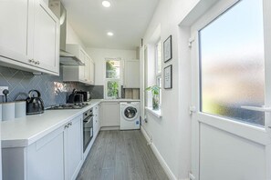 Cocina compacta con armarios blancos, lavadora y ventana con vidrio esmerilado.