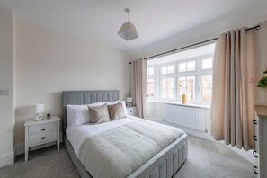 A bedroom with a bed, nightstand, lamp, window, and curtains.