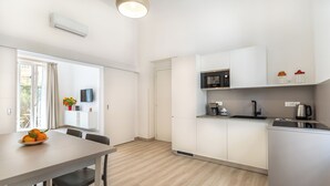 A modern kitchen with white cabinets, a microwave, and a coffee maker. There is a dining table with chairs and a window with curtains. - Brand new Central Sorrento 2 BR 2 BT Flat AC Wifi Parking Balcony (Sorrento)