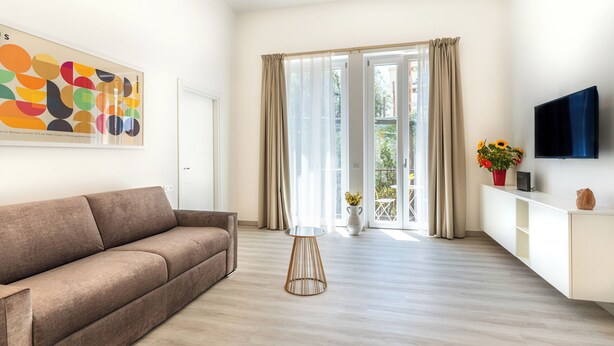 A modern living room with a sofa, a small round table, a flat-screen TV, and a large window with curtains. - Brand new Central Sorrento 2 BR 2 BT Flat AC Wifi Parking Balcony (Sorrento)
