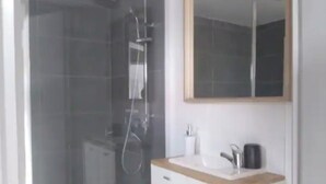 Ein modernes Badezimmer mit einer Glaskabine zur Dusche, einem weißen Waschtisch mit Holzplatte und einem großen Spiegel über dem Waschbecken.