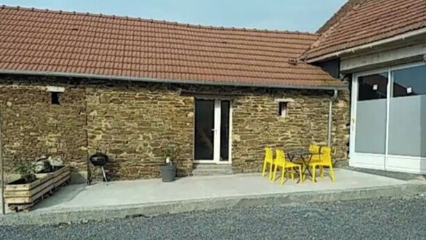 Ein Steinhaus mit Ziegeldach, einer Haustür und einer kleinen Veranda mit gelben Stühlen.