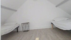 Ein kleines, dreieckiges Dachzimmer mit zwei Etagenbetten und einem Metallgestell.
