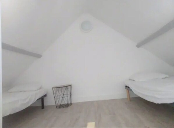 Una habitación ático pequeña y triangular con dos literas y un estante metálico.