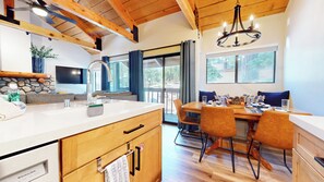 Une cuisine moderne avec des poutres en bois, un grand îlot central et un coin repas comprenant une table et des chaises.