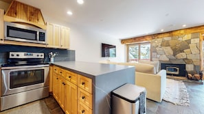 A modern kitchen with stainless steel appliances, wooden cabinets, and a stone fireplace. - Updated 2-Story Home, Great Views, Steam Shower & Washer/Dryer, Near Village (Mammoth Lakes)