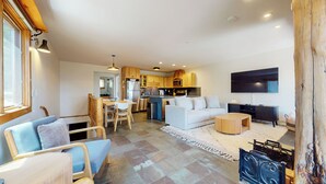 A modern kitchen with wooden cabinets, a dining area with a table and chairs, a living room with a sofa and a TV, and a large window. - Updated 2-Story Home, Great Views, Steam Shower & Washer/Dryer, Near Village (Mammoth Lakes)