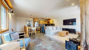 A modern kitchen with wooden cabinets, a dining area with a table and chairs, a living room with a sofa and a TV, and a large window. - Updated 2-Story Home, Great Views, Steam Shower & Washer/Dryer, Near Village (Mammoth Lakes)