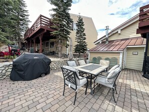 Un patio al aire libre con mesa y sillas, una parrilla y un muro de piedra.