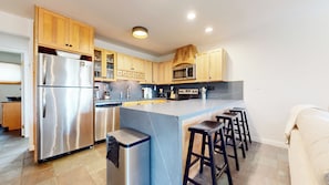 A modern kitchen with stainless steel appliances, wooden cabinets, a central island with bar stools, and a microwave above the stove. - Updated 2-Story Home, Great Views, Steam Shower & Washer/Dryer, Near Village (Mammoth Lakes)