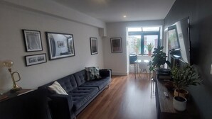 A modern living room with a dark-colored sofa, a coffee table, and a TV mounted on the wall. There are framed pictures on the wall and a potted plant on the floor. - Stylish, Comfy 1BD with Cathedral Neighbour (Dublin)