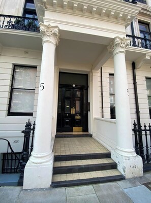 Entrada de un edificio con una puerta negra, columnas blancas y el número 5 en la pared.