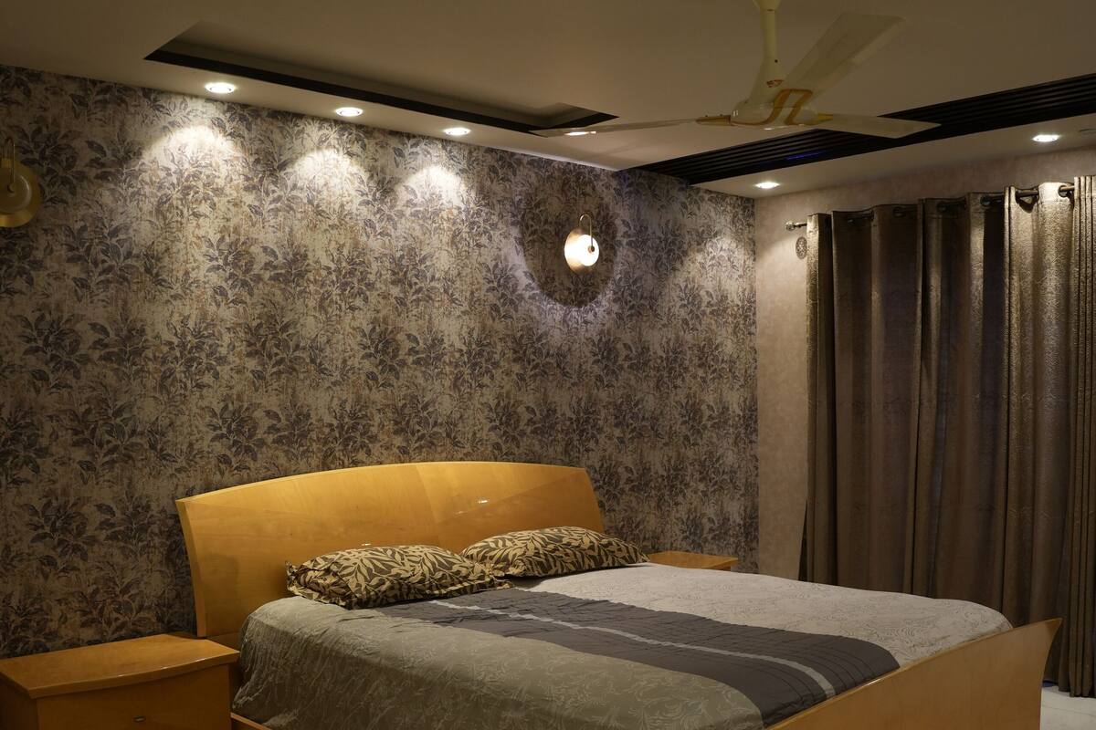Une chambre à coucher moderne avec un grand lit, une table de chevet, un ventilateur de plafond et un mur décoré d’un motif.