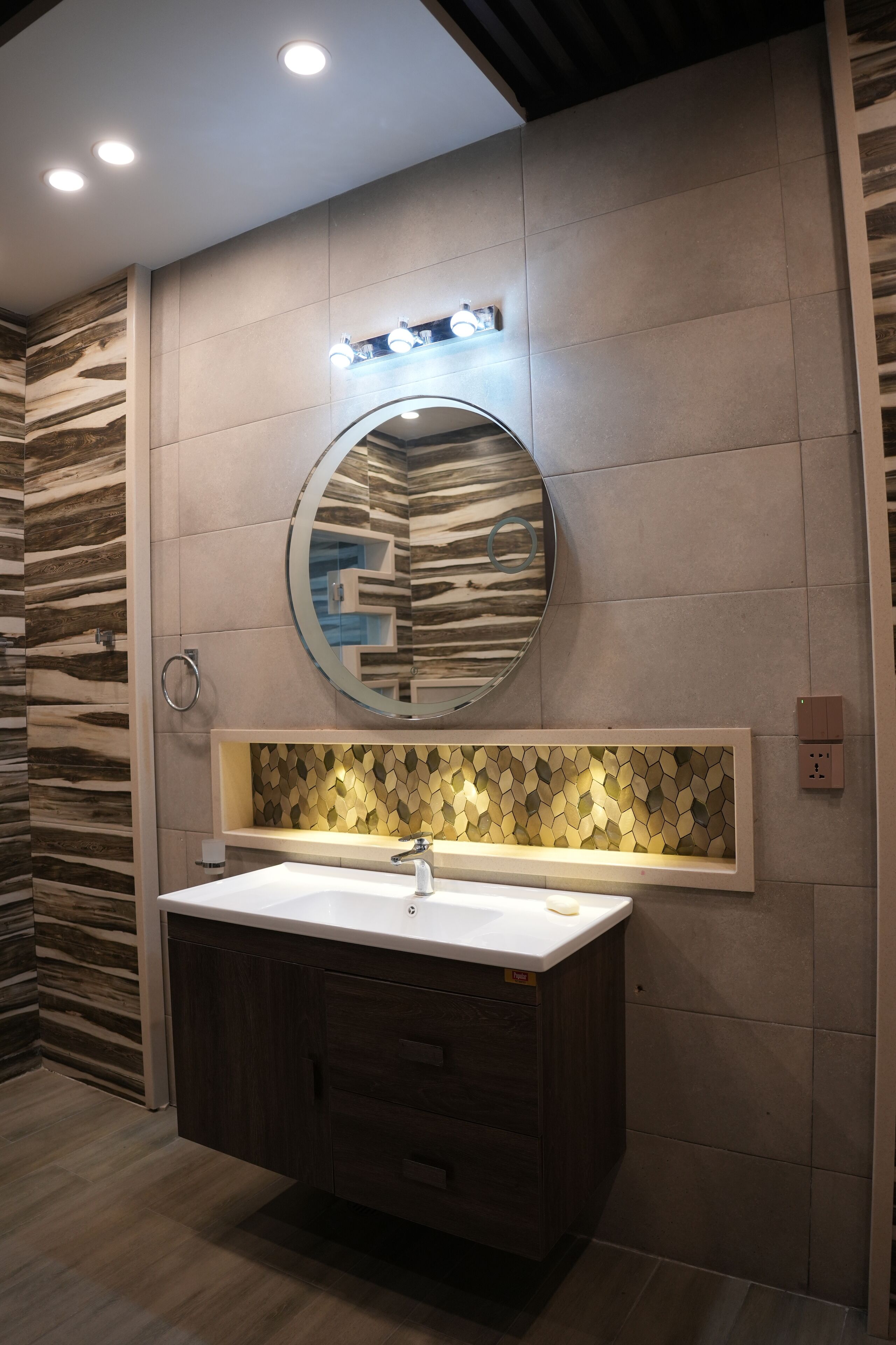 Een moderne badkamer met een ronde spiegel, een inbouw wastafel en een betegelde spatwand.