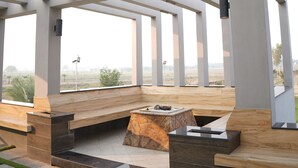 An outdoor patio area with a modern design, featuring a bench, a small table, and a fire pit. - Triphatch Farm House (Lahore)