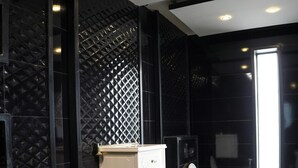 A modern bathroom with black tiled walls, a white cabinet, and a large window providing natural light. - Triphatch Farm House (Lahore)