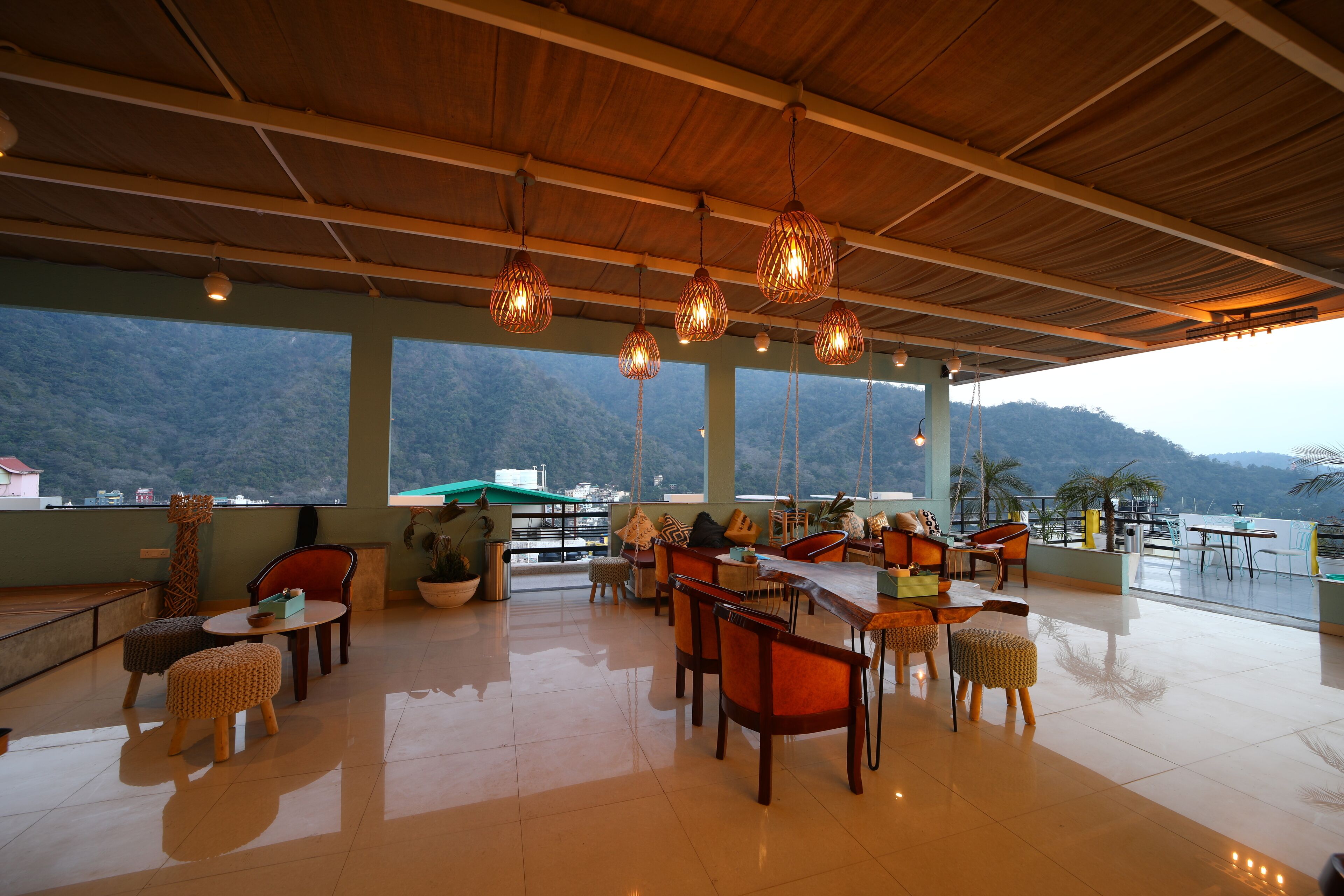 A spacious outdoor dining area with a view of the mountains, wooden ceiling, and hanging light fixtures.