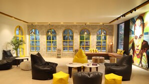 Un vaste espace salon avec des canapés en cuir, des coussins jaunes et une grande fenêtre aux arches élégantes.