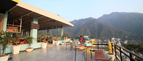 An outdoor seating area with tables and chairs, potted plants, and a view of mountains.