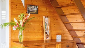 Een houten hutteruimte met een houten trap, een houten dressoir, een vaas met bloemen en een bord aan de muur.