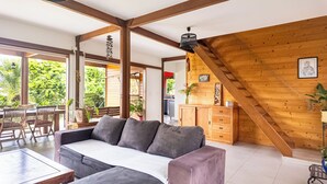 Een gezellige woonkamer met een grijze bank, houten balken en uitzicht op het landschap.