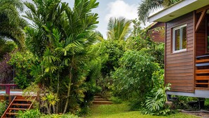 Een houten huis, omringd door weelderige begroeiing en een verzorgde tuin met een houten trap die naar het huis leidt.