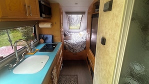 A compact RV kitchen with a sink, microwave, and a small window. - Cozy RV on 149 acres in Charleston with AC, WiFi, and eight miles of trails!


 (Charleston)