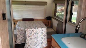 A compact RV interior with a kitchenette, a dining area with a table and chairs, and a small window. - Cozy RV on 149 acres in Charleston with AC, WiFi, and eight miles of trails!


 (Charleston)