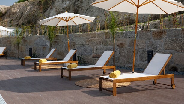 Outdoor lounge chairs with umbrellas, stone walls, and a poolside setting. - Quinta de Reis (Ponte da Barca)