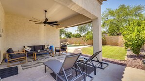A covered patio with a ceiling fan, outdoor seating, and a view of a backyard with a swimming pool and trees.