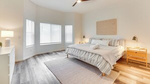 A bedroom with a bed, bedside tables, a ceiling fan, and large windows with blinds.