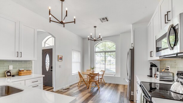 A modern kitchen with white cabinetry, a dining area with wooden chairs, and a large window providing natural light.