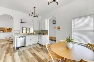 Una cocina moderna con armarios blancos, lavavajillas integrado y un comedor con mesa y sillas de madera.
