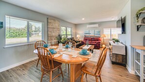 A dining area with a wooden table and chairs, a sofa, and a TV mounted on the wall. - Pet-friendly Moclips Home: Walk to Mocrocks Beach! (Moclips)