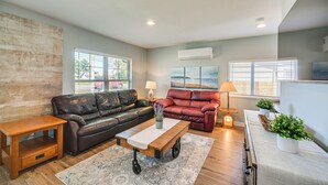 A living room with a brown leather sofa, a red sofa, a wooden coffee table, and a small side table. - Pet-friendly Moclips Home: Walk to Mocrocks Beach! (Moclips)