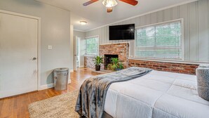 Une chambre avec une cheminée en briques, un ventilateur de plafond et un grand lit.