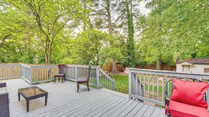 Une terrasse en bois, agréée de mobilier d’extérieur, notamment une table et des chaises à plateau en verre, le tout entouré d’une clôture en bois et d’arbres.
