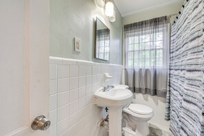 Un baño con un lavamanos blanco, un inodoro y un espejo. Hay una ventana con cortinas y una cortina de ducha a rayas.