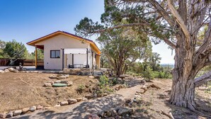 Une maison de plain-pied dotée d’un patio couvert, entourée d’un jardin aménagé avec des rochers et des arbres.