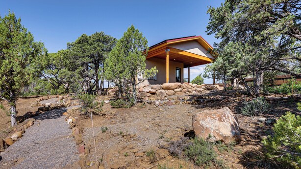 Une maison moderne avec des fondations en pierre, entourée d’arbres et bordée d’un chemin de gravier.