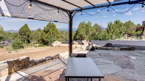 Une terrasse extérieure avec une table en pierre et un espace salon, offrant une vue sur un paysage montagneux.